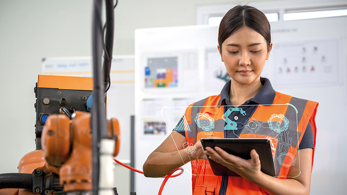 A lady wearing a safety orange vest, at a warehouse, holding a tablet showing automation technologies 