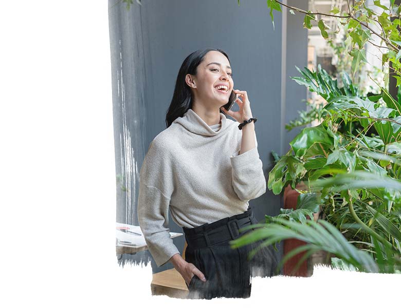A woman standing near the garden area and smiling while talking on phone