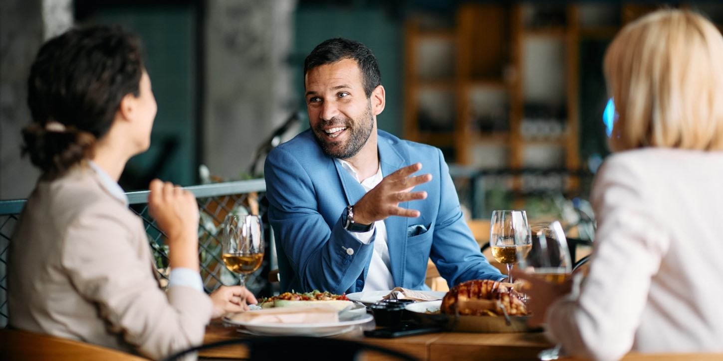 Happy entrepreneur talks to female co-workers while having business lunch
