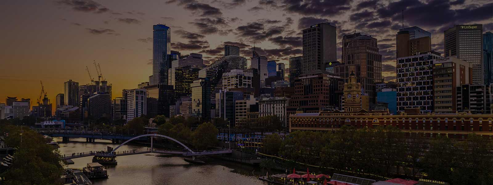 A view down the Yarra River of  Melbourne’s Southbank Cityscape during ‘golden hour’ when the sky is purple and orange with long dark grey clouds. 