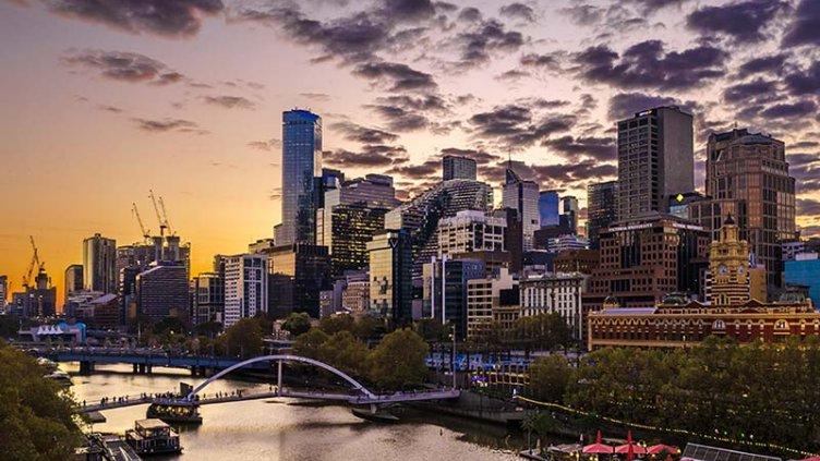 A view down the Yarra River of  Melbourne’s Southbank Cityscape during ‘golden hour’ when the sky is purple and orange with long dark grey clouds.