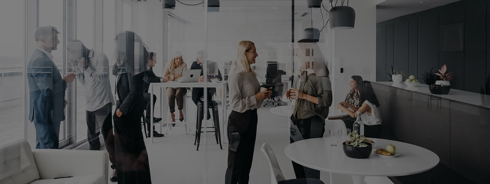 A photo of a company in everyday life in a modern office with large windows. They are smartly dressed and standing up having conversations. Horizontal daylight indoor photo.