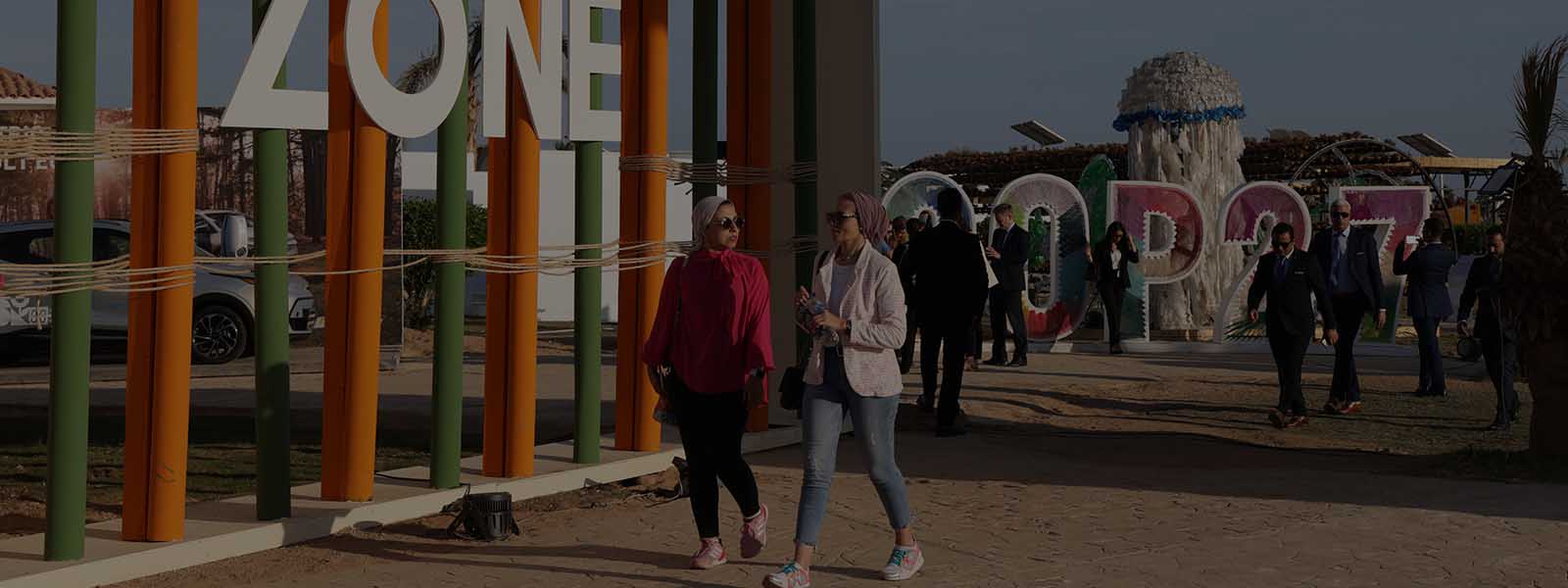 Two women walking outdoors past a large sign that says ‘Green zone’ at the Cop 27 climate change summit in Sharm El Sheikh, Egypt.