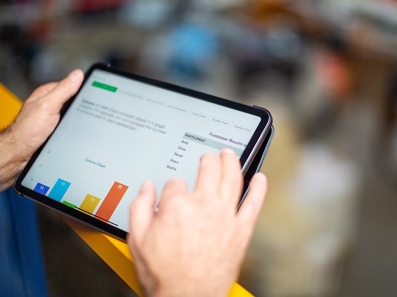 A person’s hands holding a tablet with a bar graph on the screen