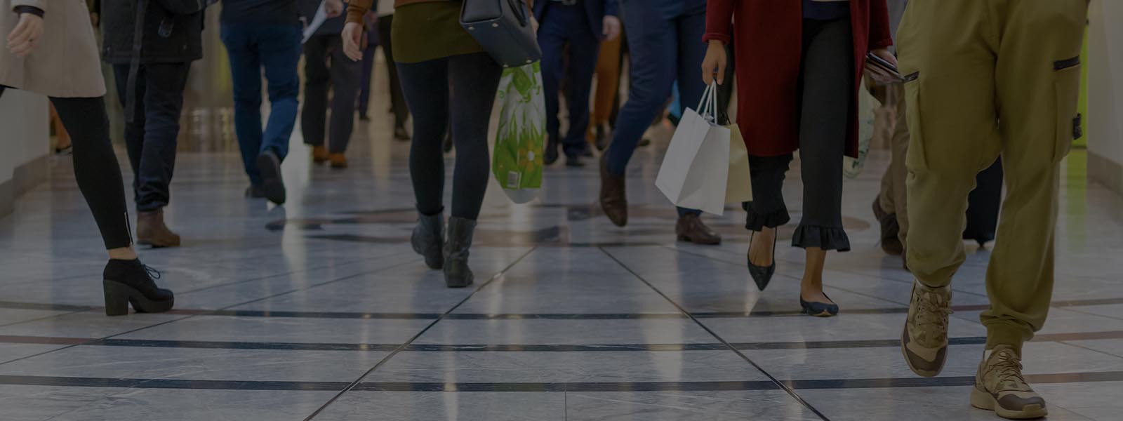A cropped picture of many pairs of legs of shoppers walking on shiny white and grey tiles in a shopping centre