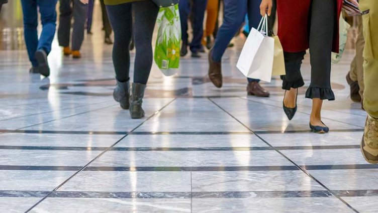 A cropped picture of many pairs of legs of shoppers walking on shiny white and grey tiles in a shopping centre