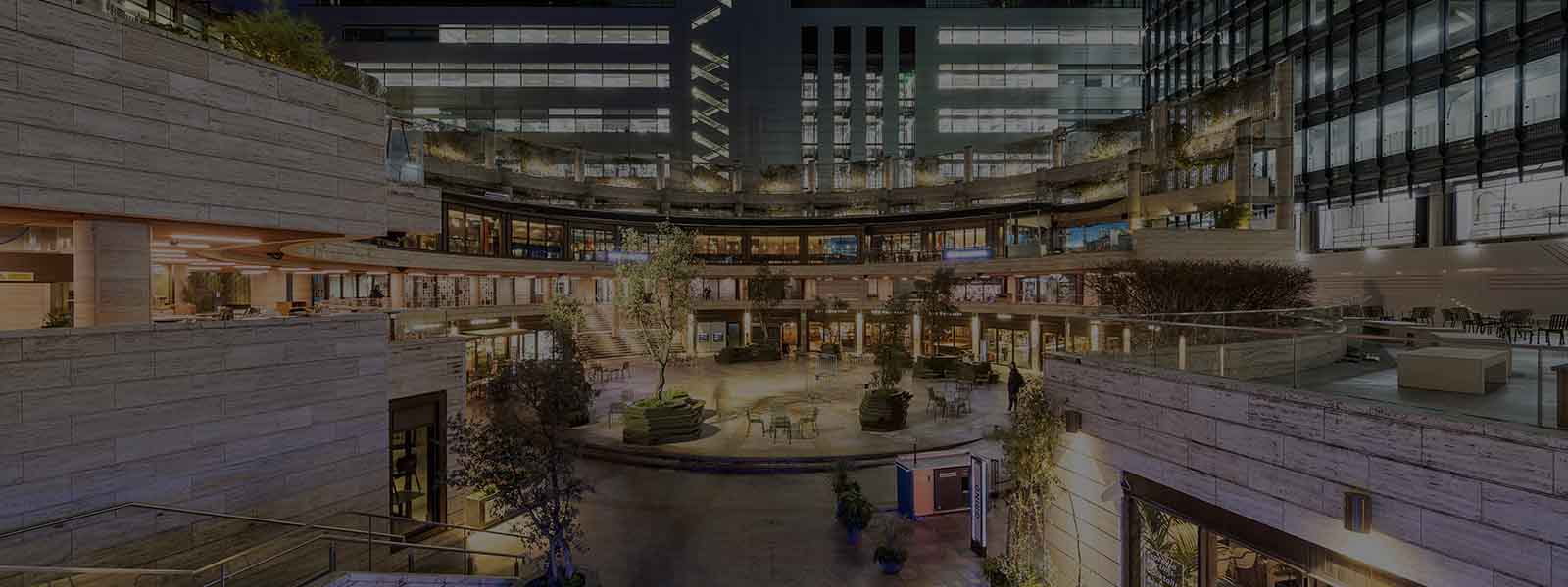 A picture of the Broadgate Circle redevelopment in London at night time, including landscaping, with ambient purple, white and yellow lighting. 