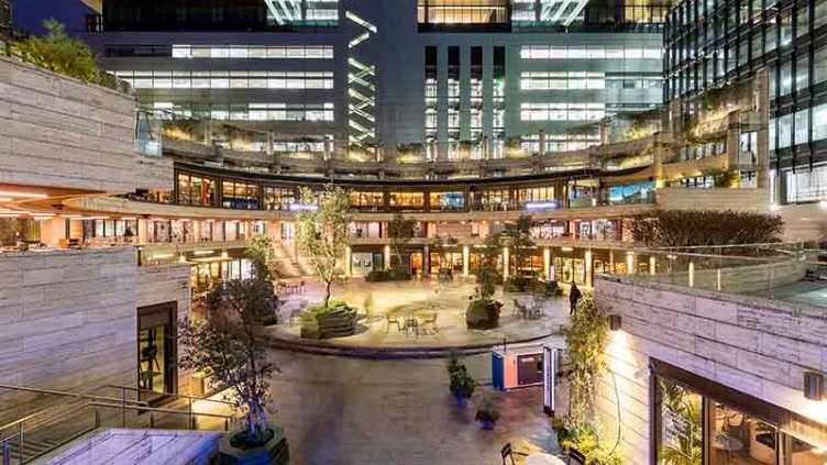 A picture of the Broadgate Circle redevelopment in London at night time, including landscaping, with ambient purple, white and yellow lighting. 