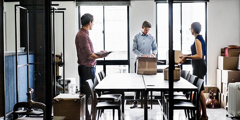 Two men and a woman unpacking boxes in an office.