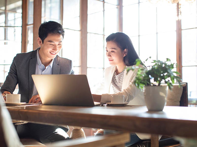 Two professionals smiling and working on new strategies using a laptop while sitting in the office workplace