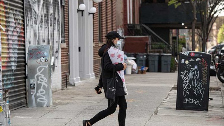 A woman walking on road while wearing a mask and carrying flower bouquet