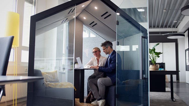 Colleagues working on laptop sitting in office cubicle