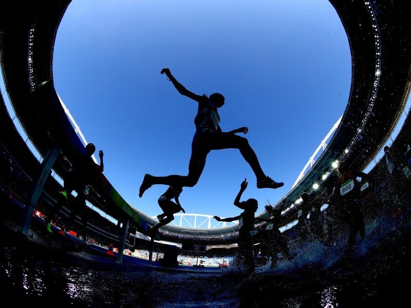 Silhouette of athletes leaping into the air inside an Olympic stadium