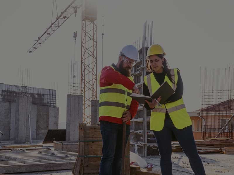 Man and woman in hard hats and high vis vests on a construction site looking at a laptop