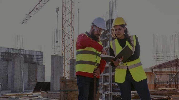 Man and woman in hard hats and high vis vests on a construction site looking at a laptop