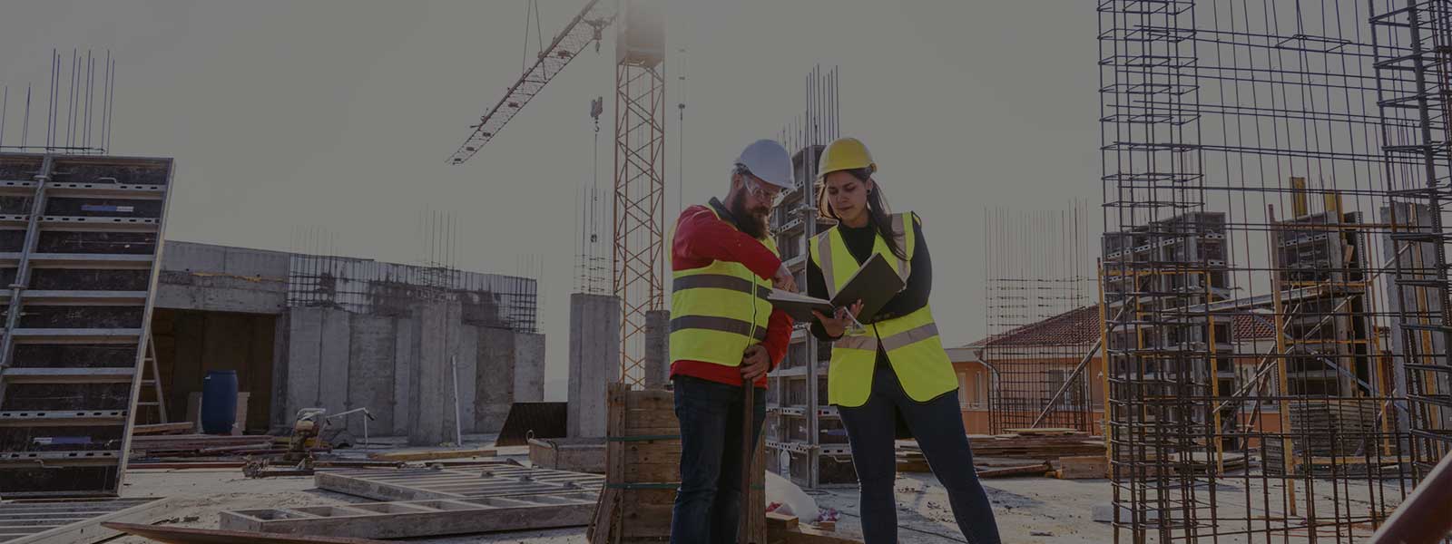 Man and woman in hard hats and high vis vests on a construction site looking at a laptop