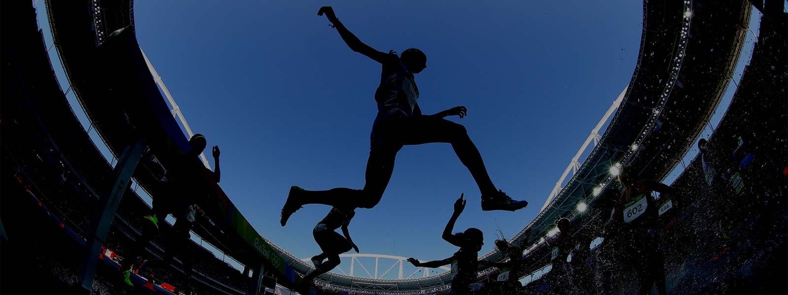 Silhouette of athletes leaping into the air inside an Olympic stadium
