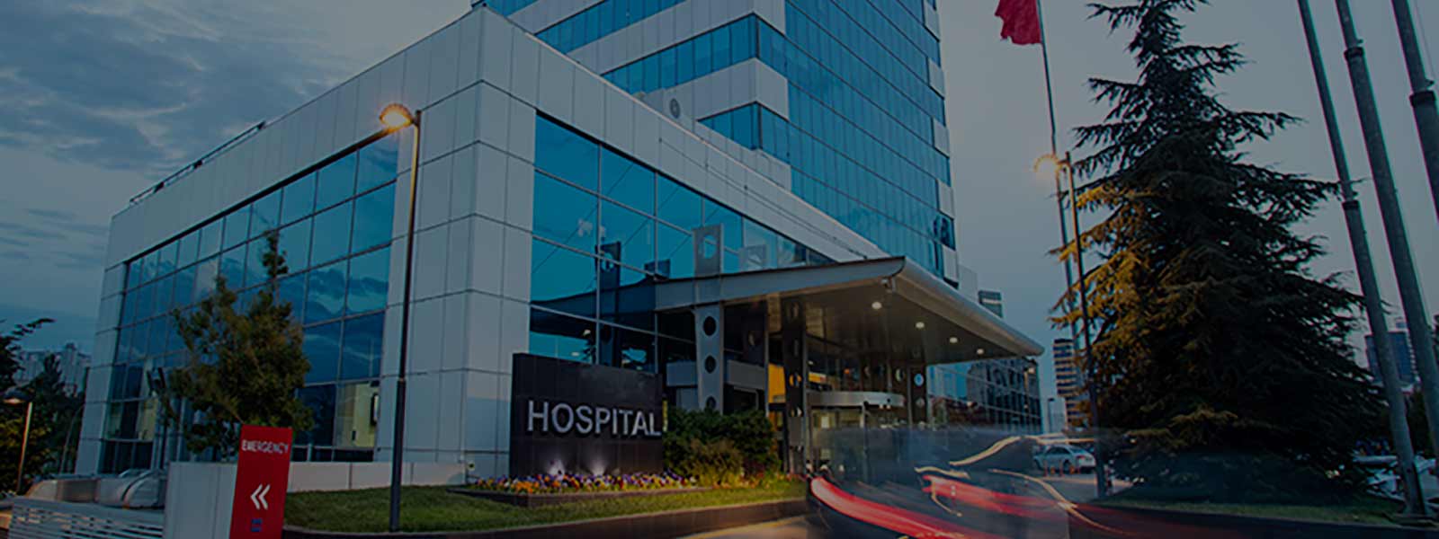 Tall modern hospital building with blurred car lights on the entrance road